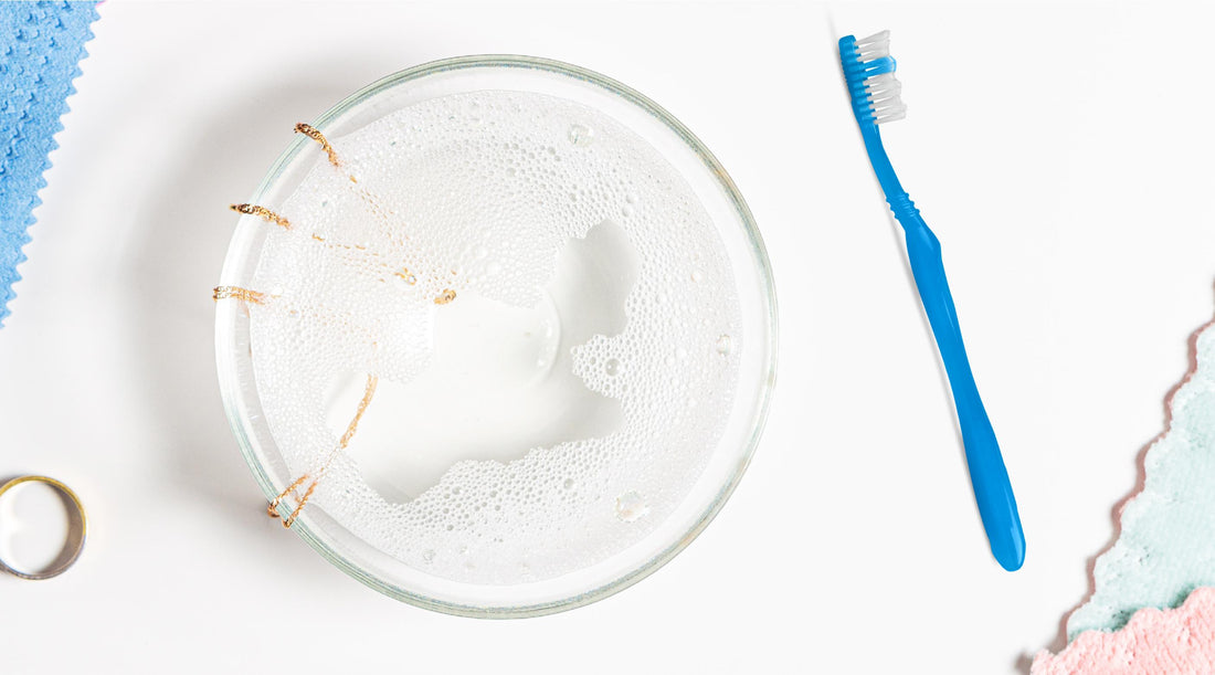 Picture of jewelry cleaning with a bowl of necklaces soaking in mild detergent and a soft toothbrush aside.