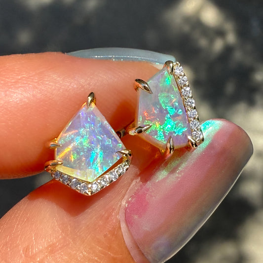 Australian Opal Earrings by NIXIN Jewelry are seen in a close-up perspective held in sunlight, revealing the intricate details of their custom 14k gold settings. This unique fine jewelry showcases rare, natural crystal opals with an extraordinary play-of-color, held by polished claw prong setting, set alongside delicate pavé diamonds.