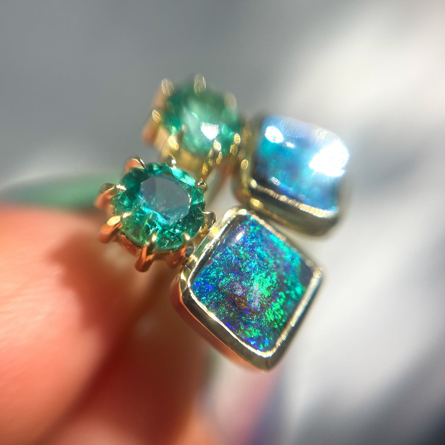Close up of Australian Opal Earrings by NIXIN Jewelry. Shows the varied tones of the blue opal and the claw prongs around the emerald.