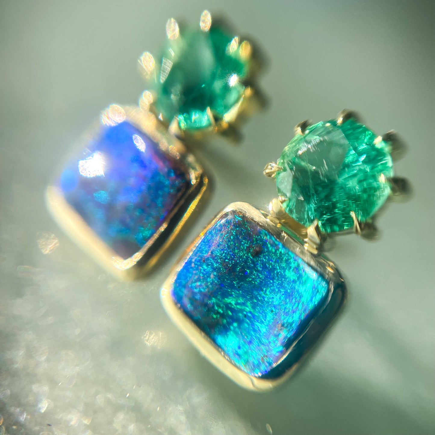 Close up of Australian Opal Earrings by NIXIN Jewelry. Luxury earrings made with Boulder Opal and emeralds in 14k gold.