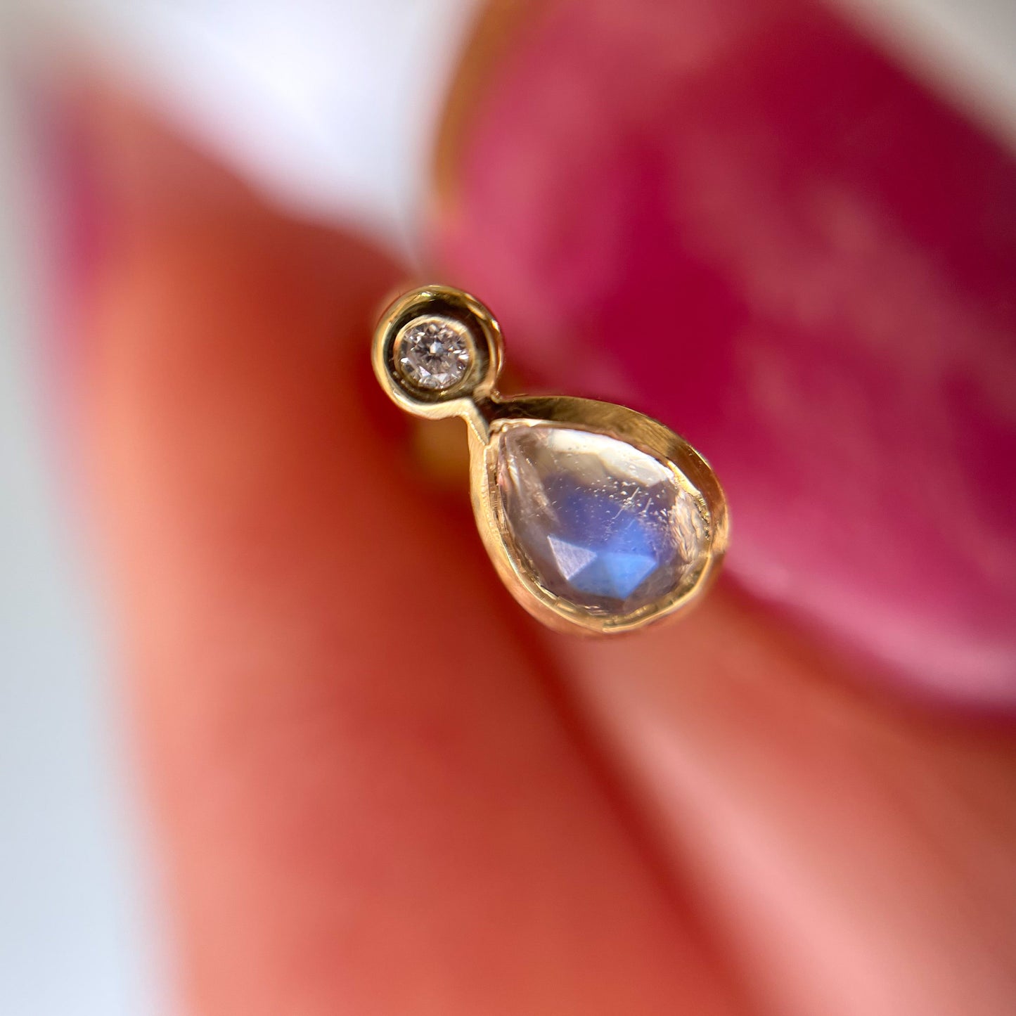 Close up of Moonstone Earrings by NIXIN Jewelry. Picture shows a magnified single blue moonstone and diamond earring held between the fingers.