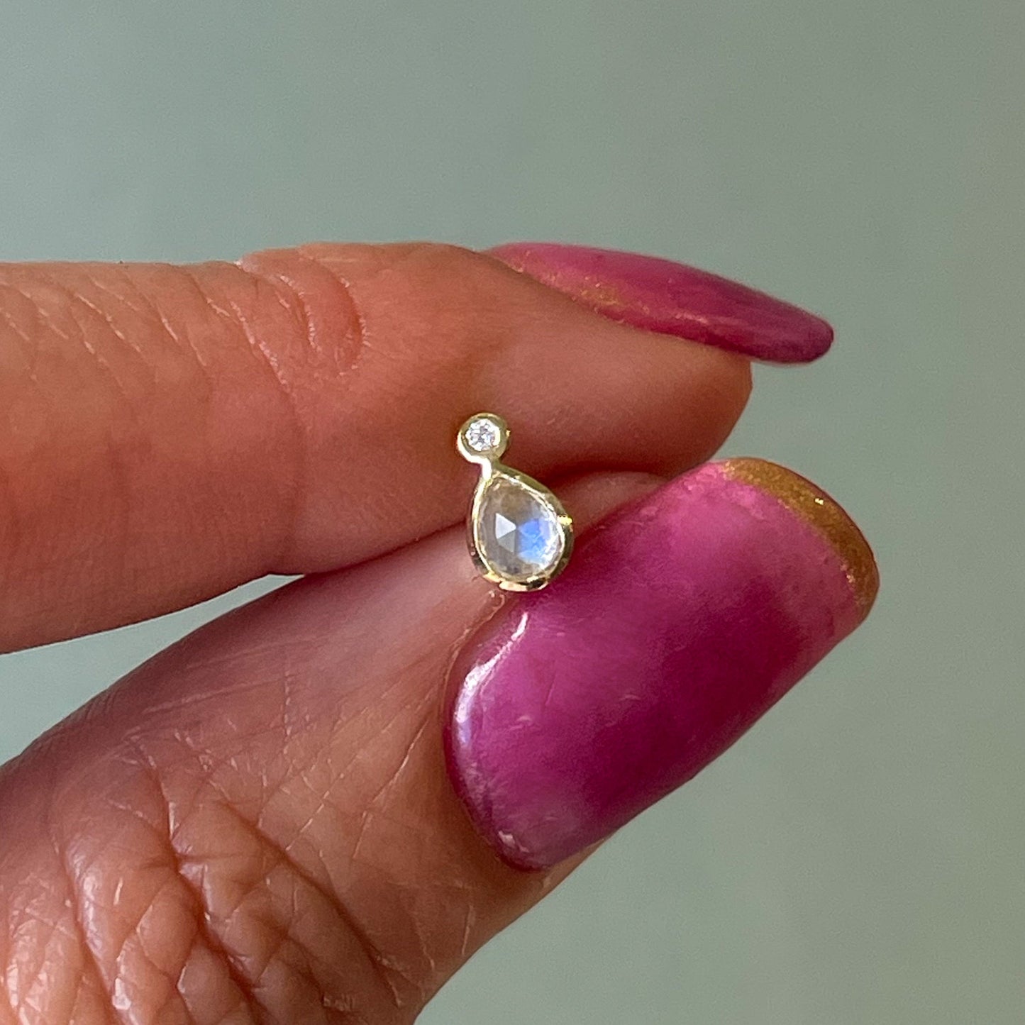 Moonstone Earrings by NIXIN Jewelry held between fingers. Showing a single stud with blue moonstone and diamond.