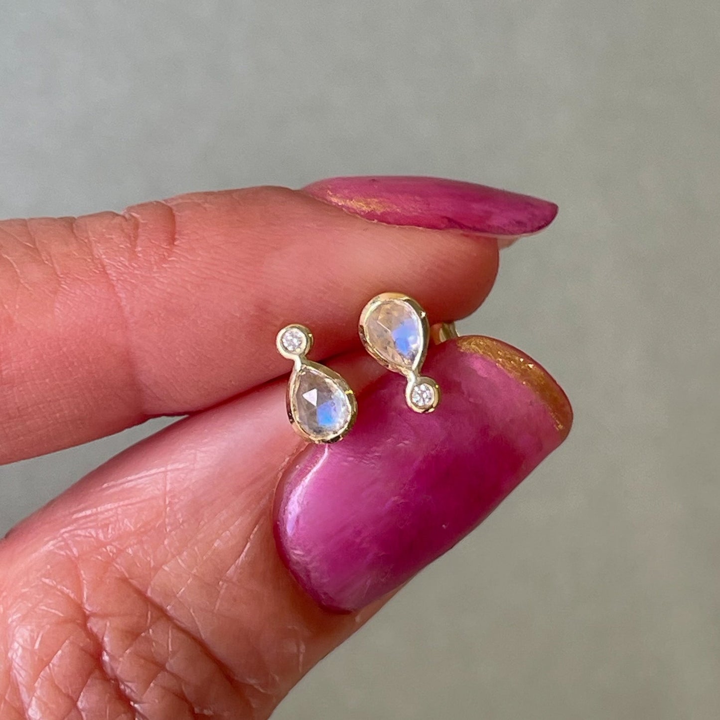 Moonstone Earrings by NIXIN Jewelry held above a glass table. Moonstone stud earrings made in yellow gold with diamonds.