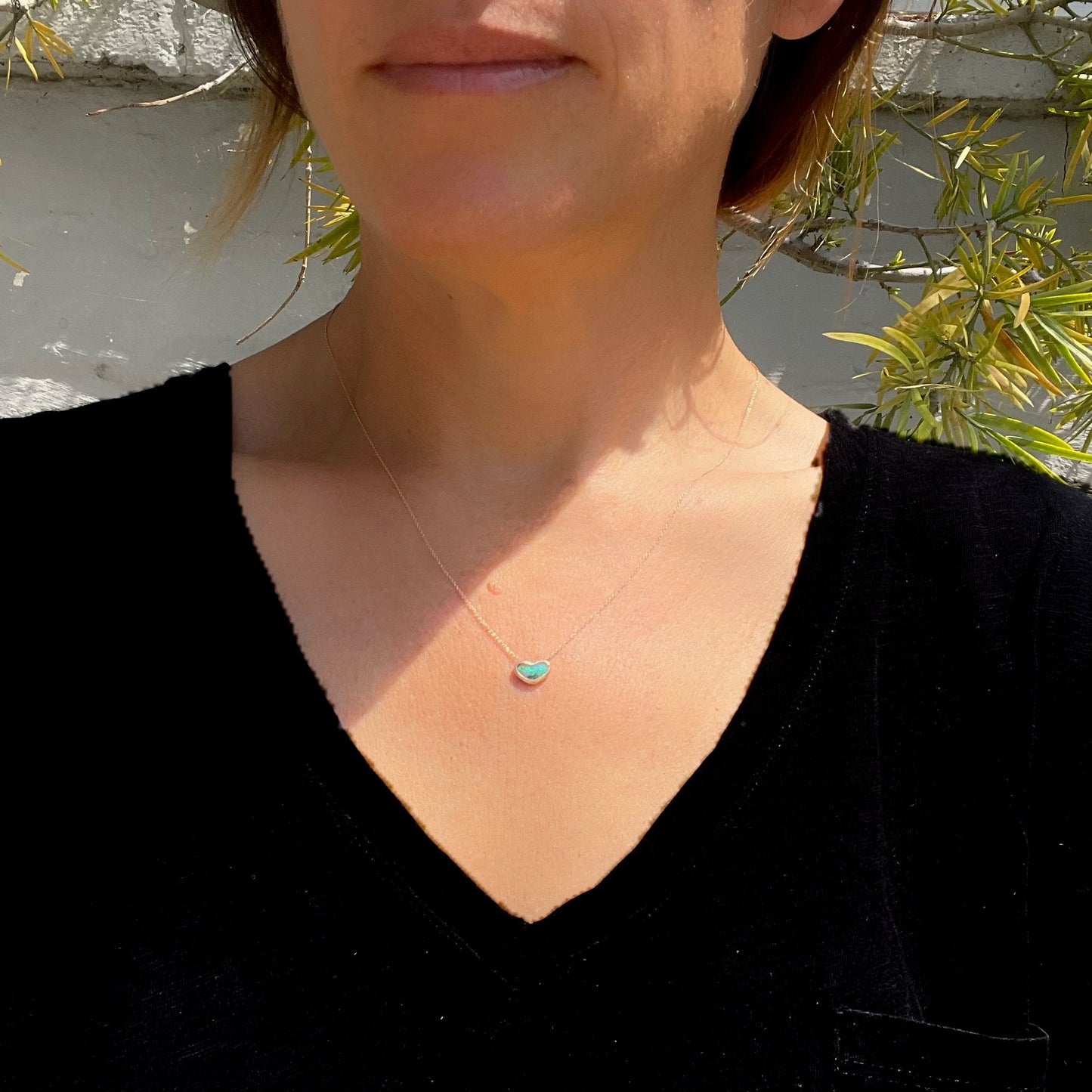 Model wearing an Australian Opal Necklace by NIXIN Jewelry. The opal pendant necklace is made in 14k rose gold.