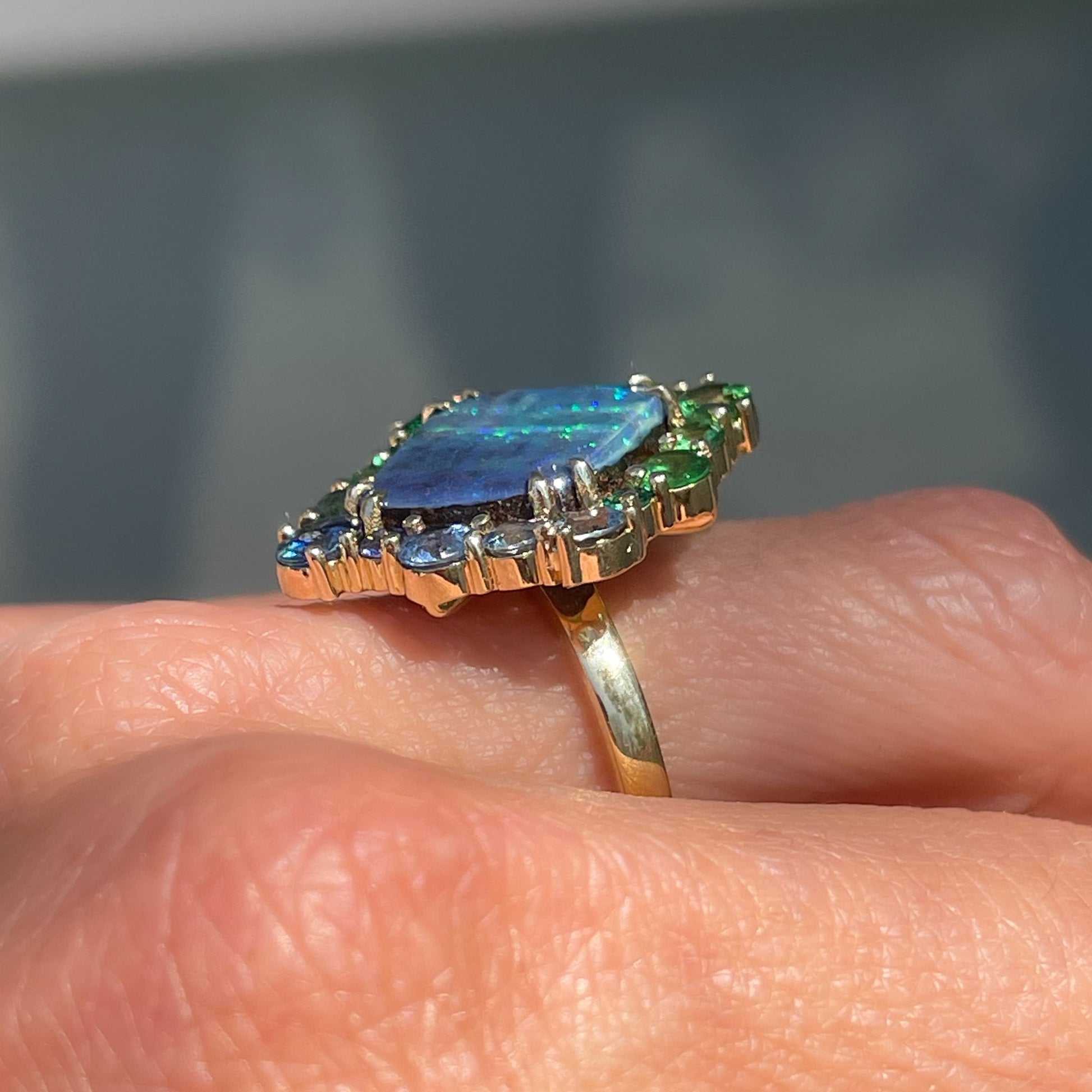 Profile shot of an Australian Opal Ring by NIXIN Jewelry, showing the halo of blue sapphires and green garnets around the opal.