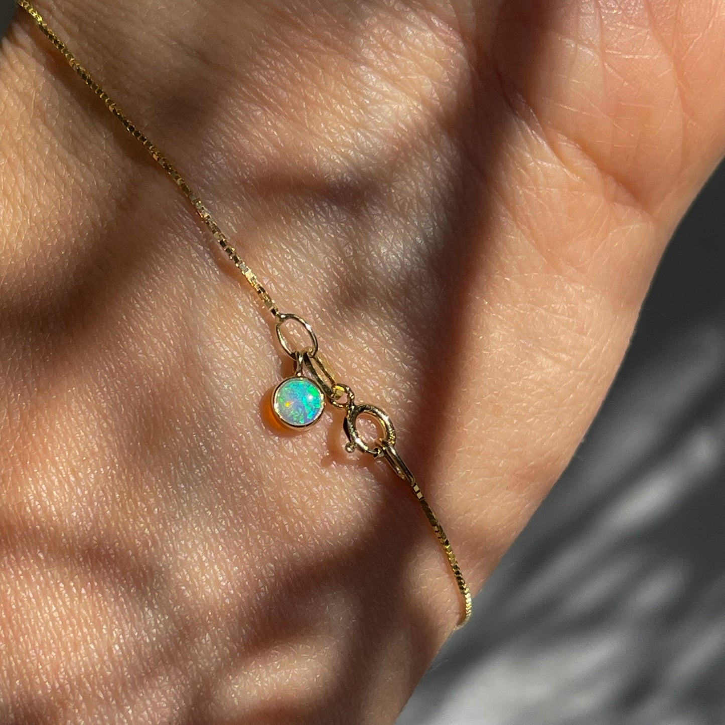 An Australian Opal Bracelet by NIXIN Jewelry shown up close against the wrist. The box chain bracelet is 14k yellow gold with a green opal.