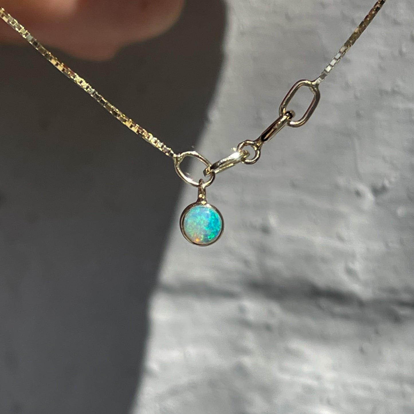 An Australian Opal Bracelet by NIXIN Jewelry shown hanging in front of a grey wall. The blue opal dangles from a simple bracelet.