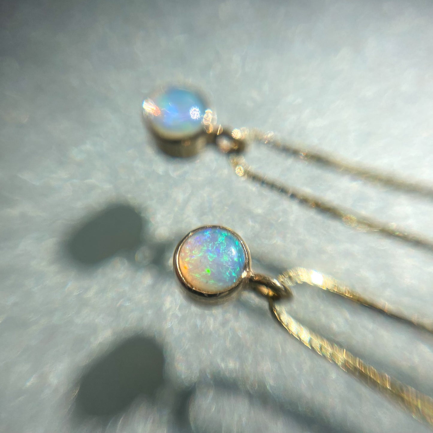 Two Australian Opal Necklaces by NIXIN Jewelry rest atop a glass tabletop. The natural opals flash blue and green.