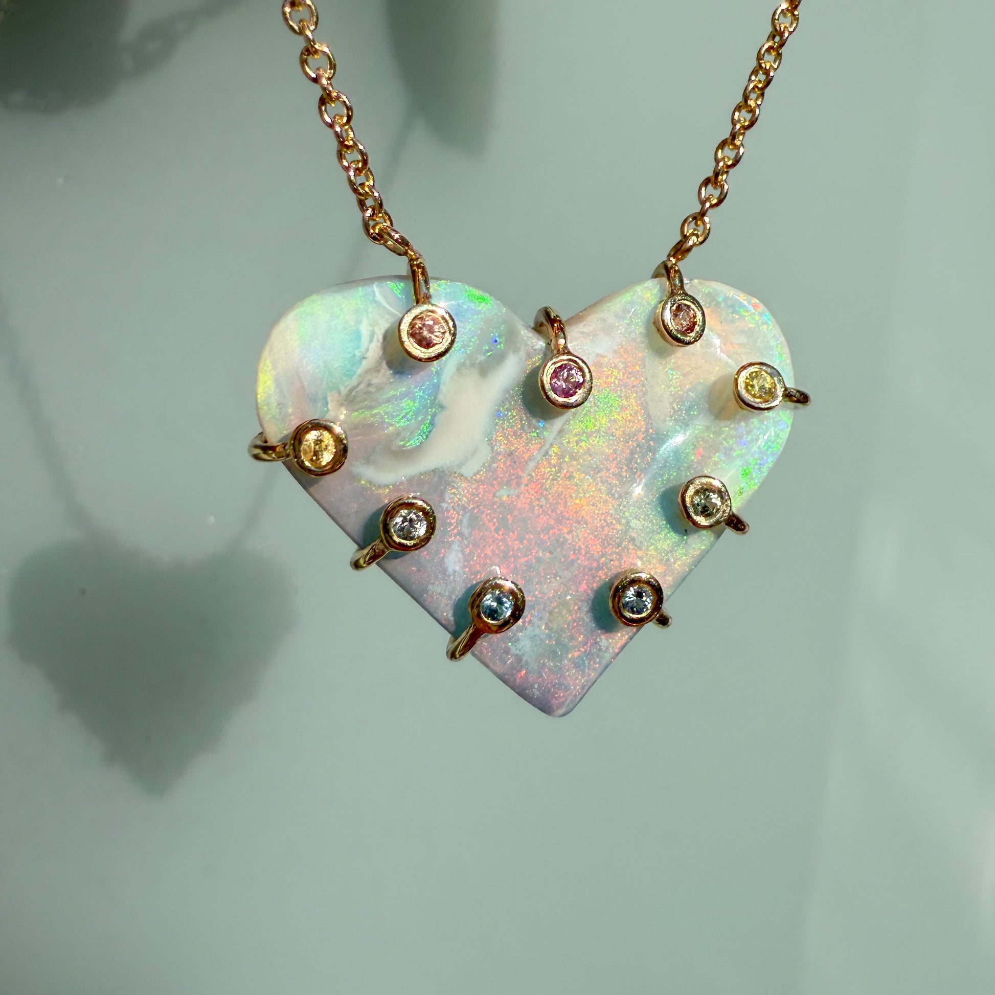 An Australian Opal Necklace by NIXIN Jewelry featuring a semi black opal pendant secured by a prong setting. The gold setting is accented with pink and yellow sapphires to create a bold piece of unique fine jewelry. This women's luxury necklace showcases a lightning ridge opal.