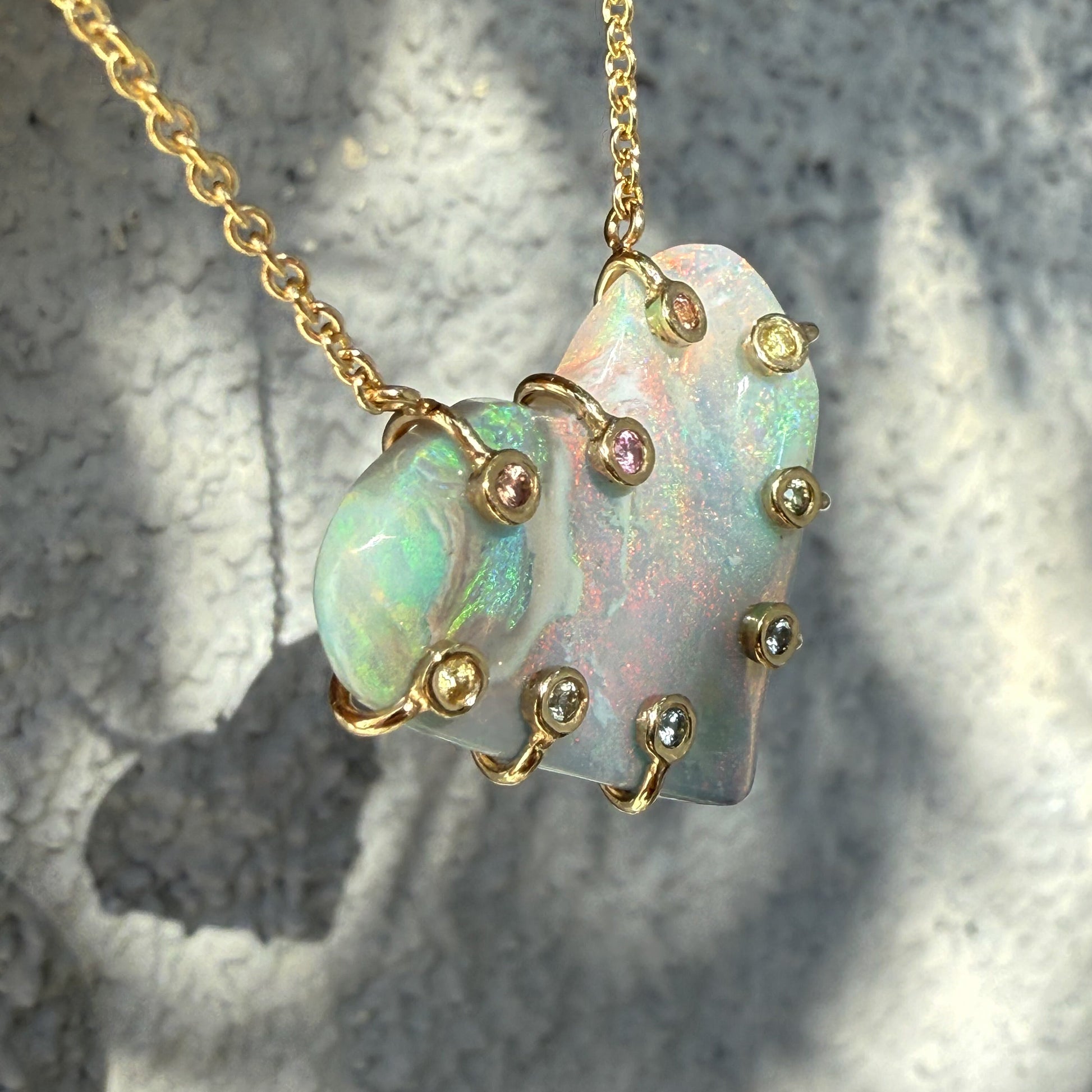 An Australian Opal Necklace by NIXIN Jewelry showcasing a close-up profile of the dimensional gold setting and the thickness of the opal pendant. The hybrid prong setting features contrasting pink sapphire and yellow sapphire details. This unique opal jewelry emphasizes the art of the setting design.