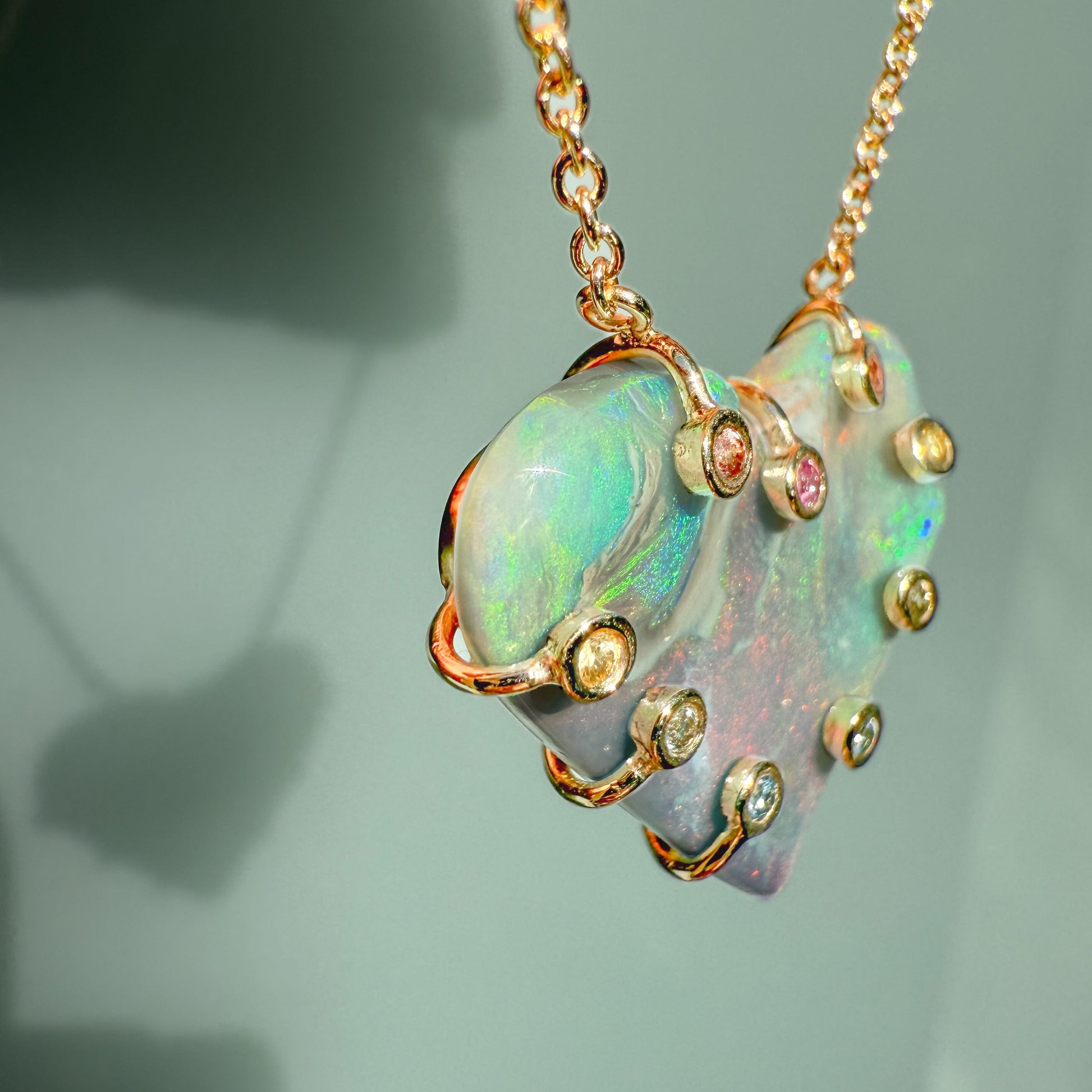 An Australian Opal Necklace by NIXIN Jewelry focusing on the bright green and blue opal fire  across the top of the heart opal pendant. The thick gold prong setting surrounds the lightning ridge opal. This stunning luxury jewelry piece is an example of artisan jewelry.