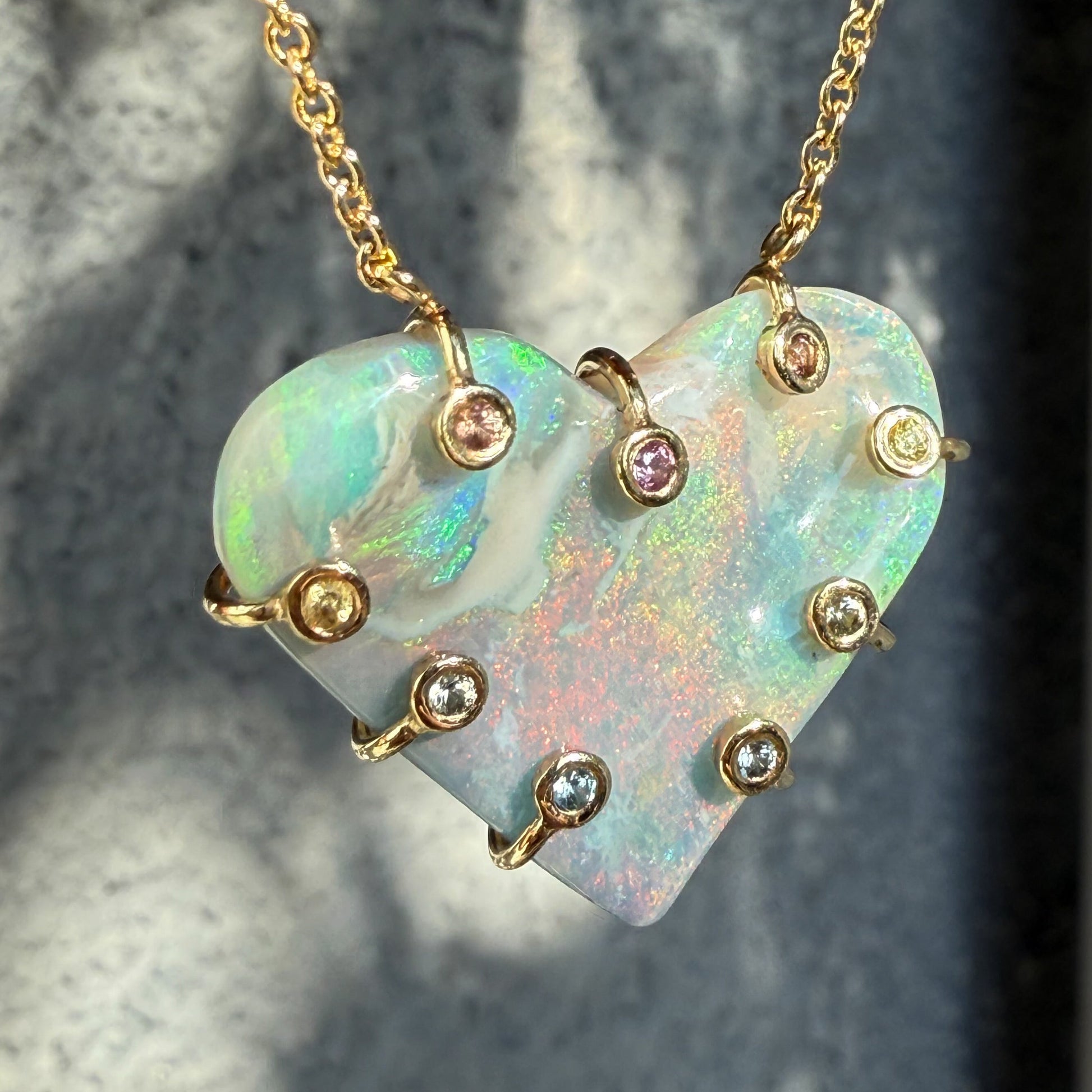An Australian Opal Necklace by NIXIN Jewelry featuring the large heart-shaped opal pendant in ambient light. The unique fine jewelry piece exhibits pink, blue and green flashes that remain vibrant against the semi black opal. This is a rare opal necklace made with natural opal.