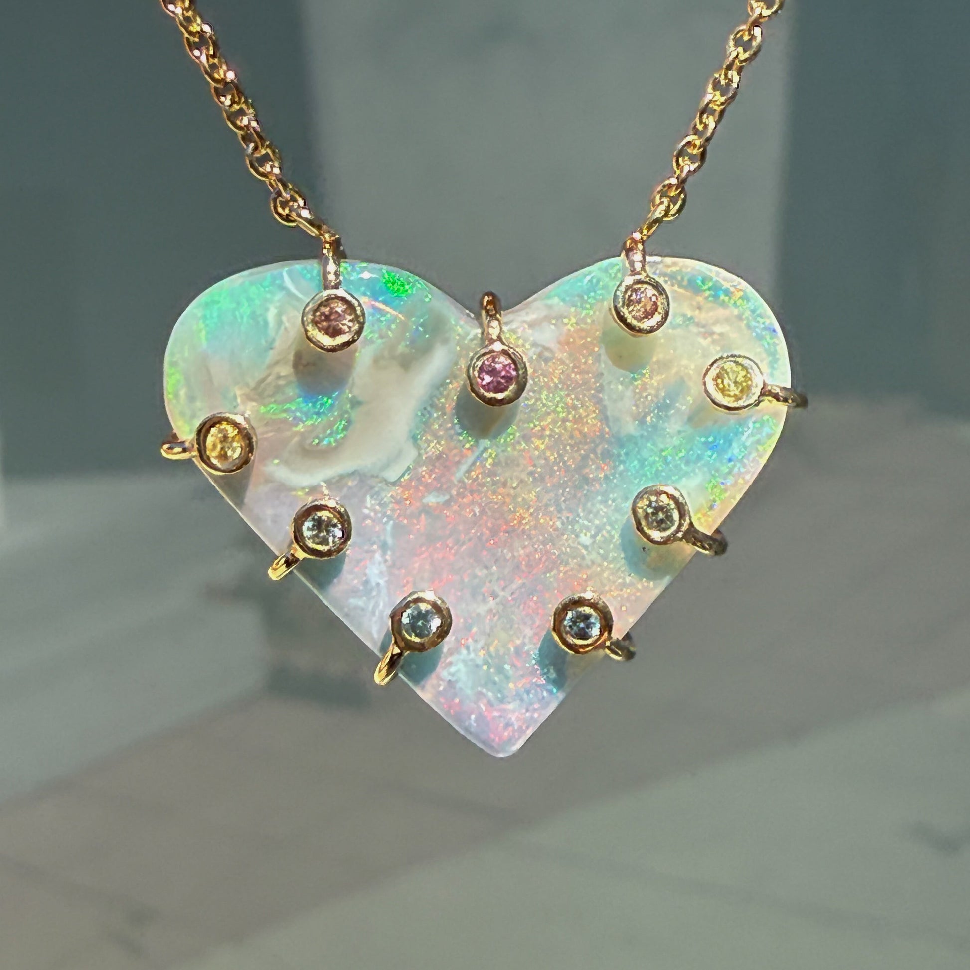 An Australian Opal Necklace by NIXIN Jewelry showing the exquisite flash of the dark opal stone in a close-up. The opal and sapphire hybrid setting highlights the rare opal jewelry. This elegant opal pendant necklace is a unique piece of jewelry art.