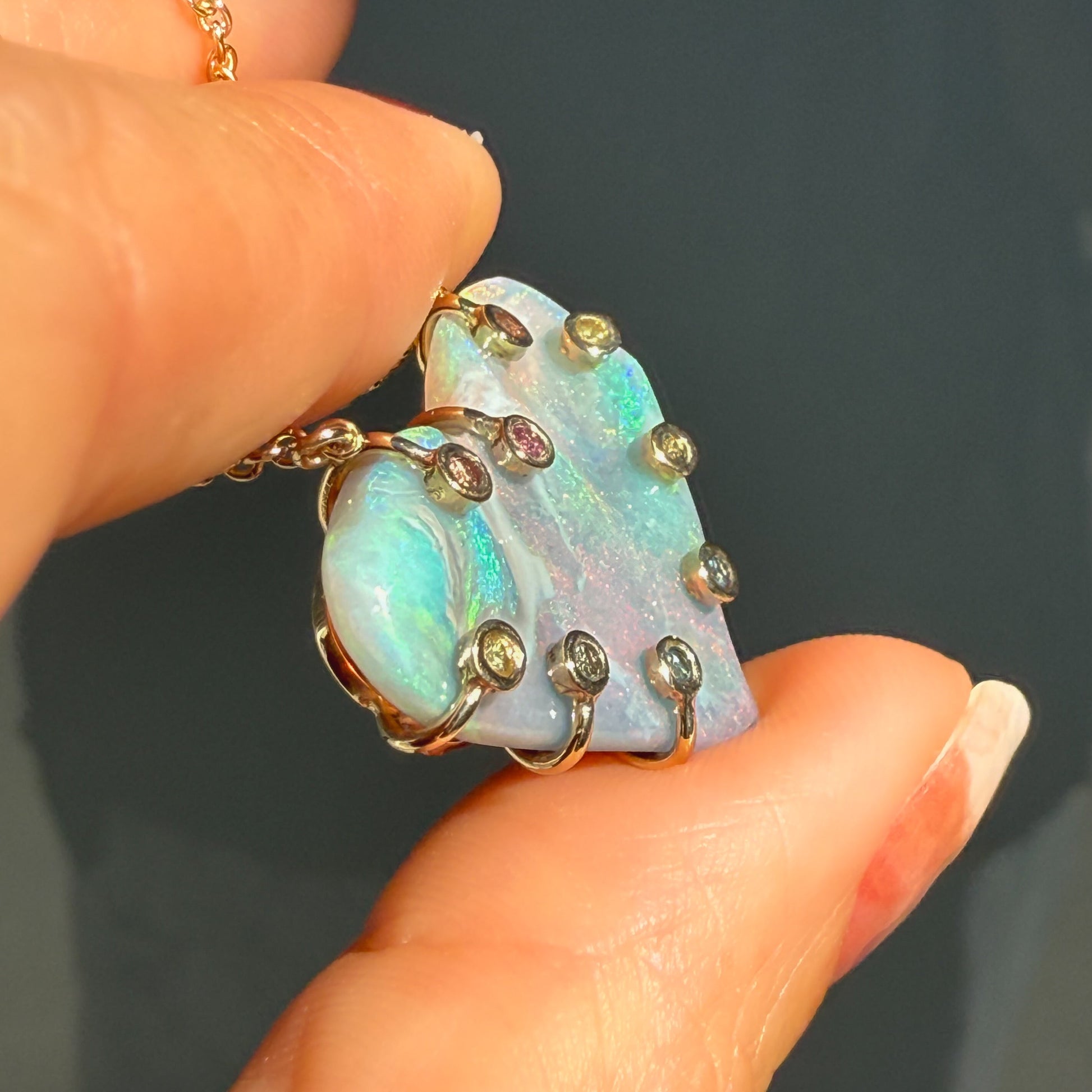 An Australian Opal Necklace by NIXIN Jewelry showcasing the unique construction of the gold opal necklace from a side angle. The unique opal jewelry design uses sapphires set within the prongs that secure the semi black opal. This high-end women's luxury necklace is truly rare jewelry.
