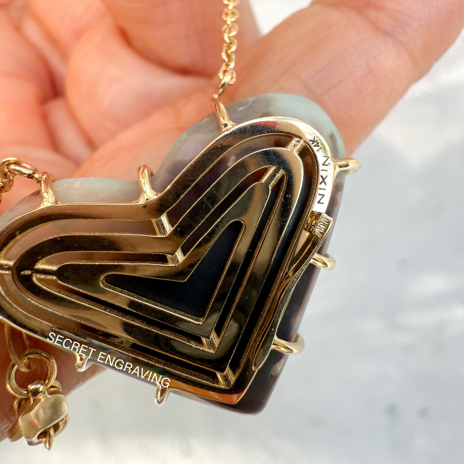 An Australian Opal Necklace by NIXIN Jewelry showing the intricate back gallery of the opal pendant. The jewelry art piece features a concentric gold opal necklace gallery and displays the maker's mark. This view highlights the unique prong setting used to secure the semi black opal.