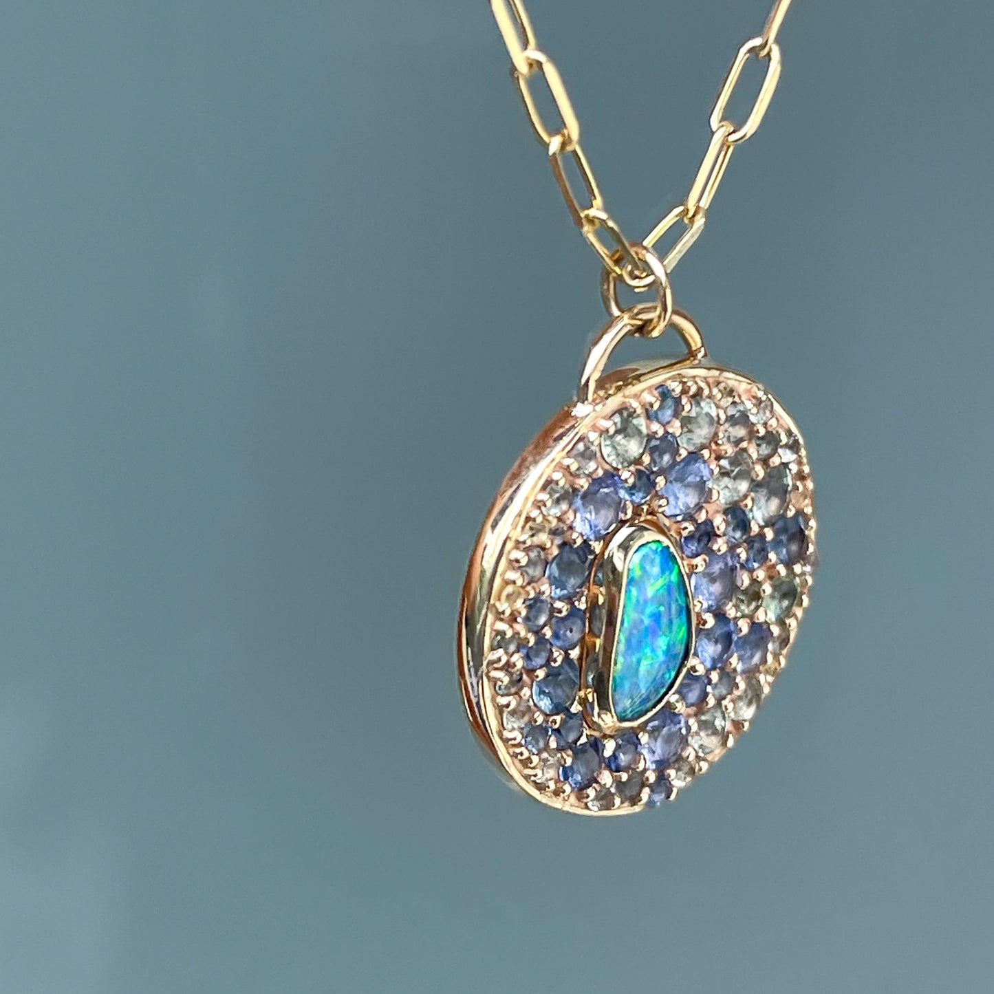 An Australian Opal Necklace by NIXIN Jewelry featuring a vivid blue opal and surrounding sapphires in bezel and prong setting. This piece of unique jewelry combines the radiance of rare gemstones with the elegance of a luxury necklace.