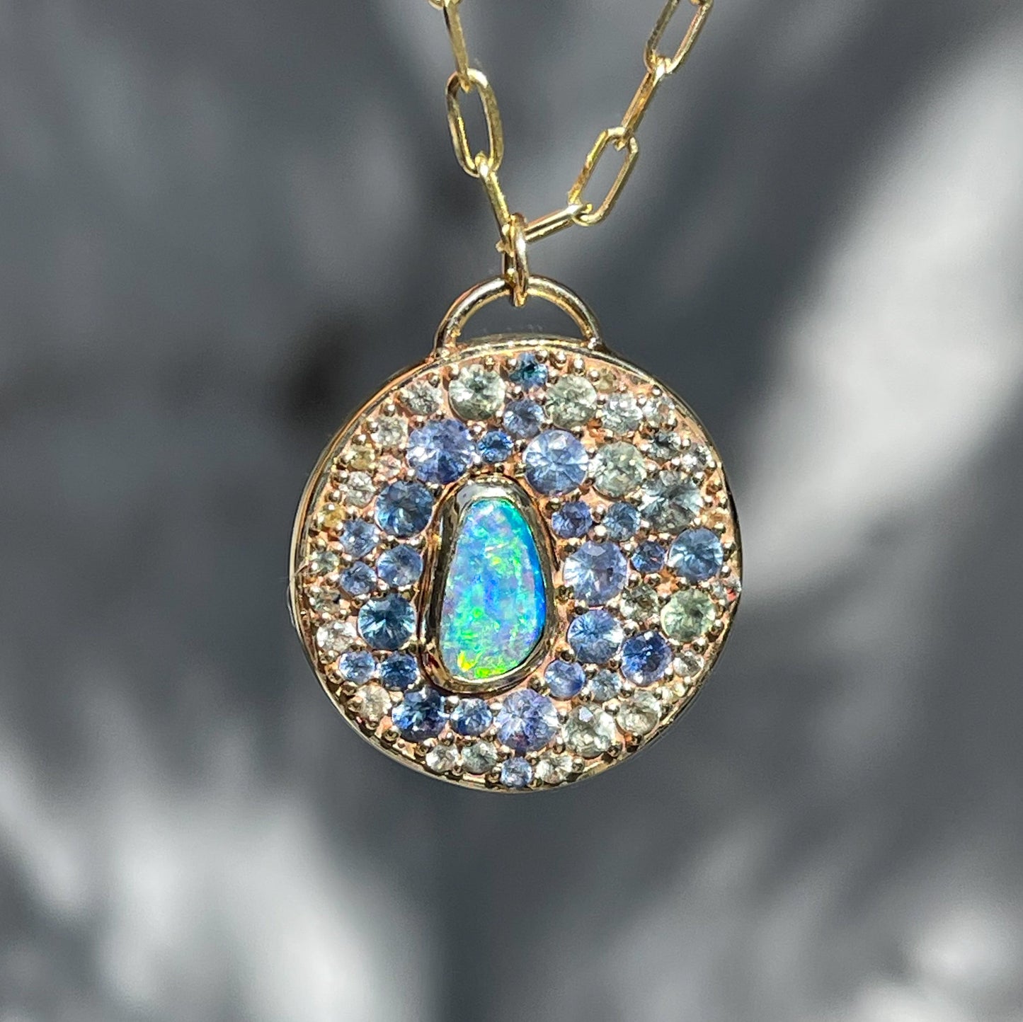 An Australian Opal Necklace by NIXIN Jewelry with a vibrant blue opal in a bezel setting. This gold opal necklace combines jewelry art and luxury design with an array of sapphires in a sophisticated layout.