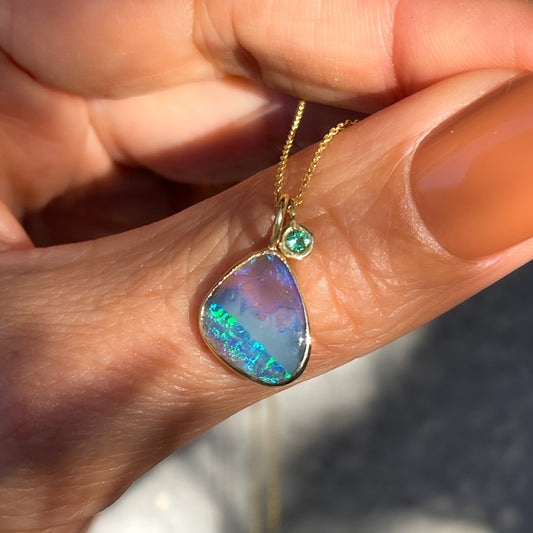 An Australian Opal Necklace by NIXIN Jewelry with a black opal in a bezel setting and a small emerald pendant.