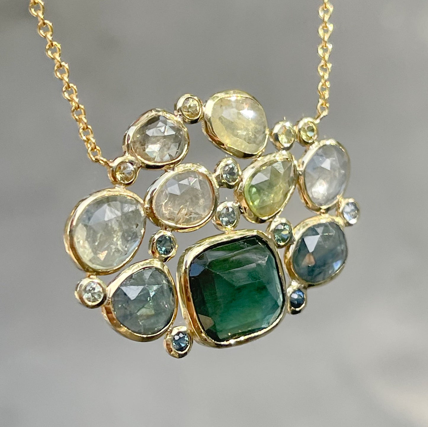 Angled shot of a Tourmaline and Sapphire Necklace by NIXIN Jewelry with muted green gemstones in bezel settings.