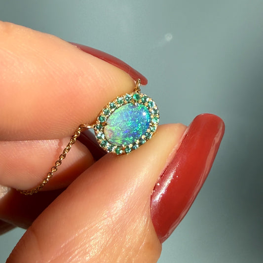 An Australian Opal Necklace by NIXIN Jewelry held to showcase a vibrant Lightning Ridge opal with an emerald halo. This luxury necklace features a rare opal pendant set in 14k gold with a high polish finish. It is a piece of unique fine jewelry designed for collectors of wearable jewelry art and high-end statement pieces.