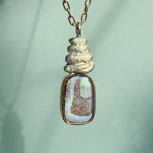 This front-facing view features an Australian Opal Necklace by NIXIN Jewelry with hand-carved and stacked, textured silver beach rocks. The luxury pendant combines the warmth of a rose gold opal necklace with the cool texture of artisan-crafted silver. It represents a piece of jewelry art that stands out as a truly unique opal jewelry investment.