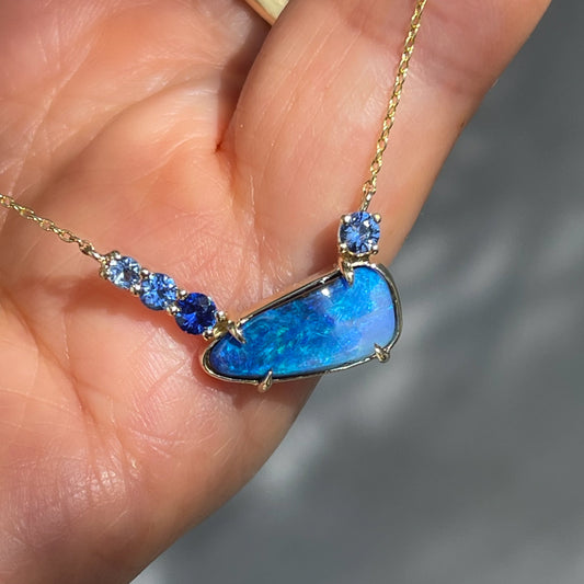 An Australian Opal Necklace by NIXIN Jewelry showcases a vibrant blue opal with ombré sapphires in a bezel setting. A perfect piece of rare jewelry and refined luxury.