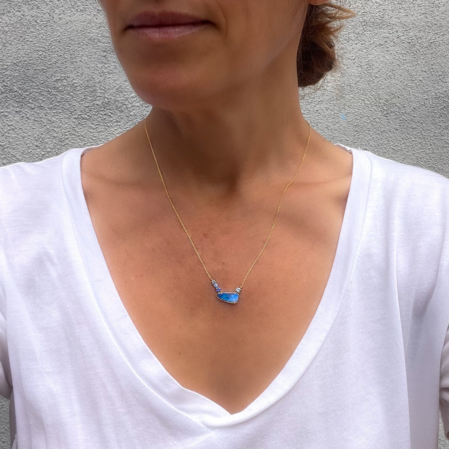 Model wearing an Australian Opal Necklace by NIXIN Jewelry. Shows the brilliance of a blue opal paired with tonal sapphires. This luxury necklace is a modern heirloom and part of unique fine jewelry collections.