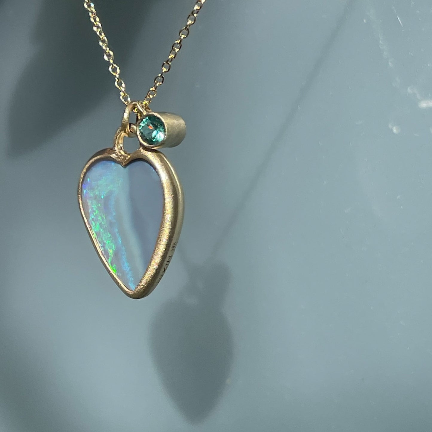 Side view of an Australian Opal Necklace by NIXIN Jewelry with an opal heart and emerald charm.