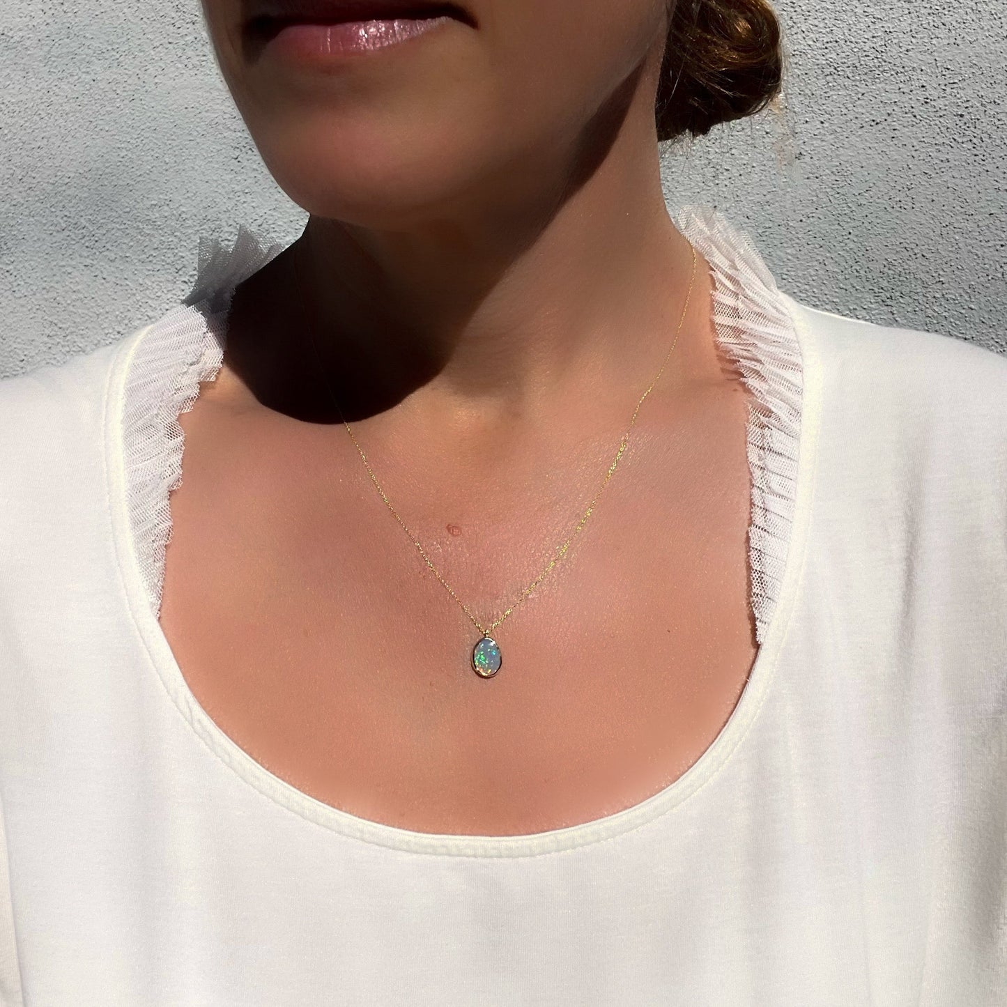 A model wearing an Australian Opal Necklace by NIXIN Jewelry with a Black Opal set in 14k gold.