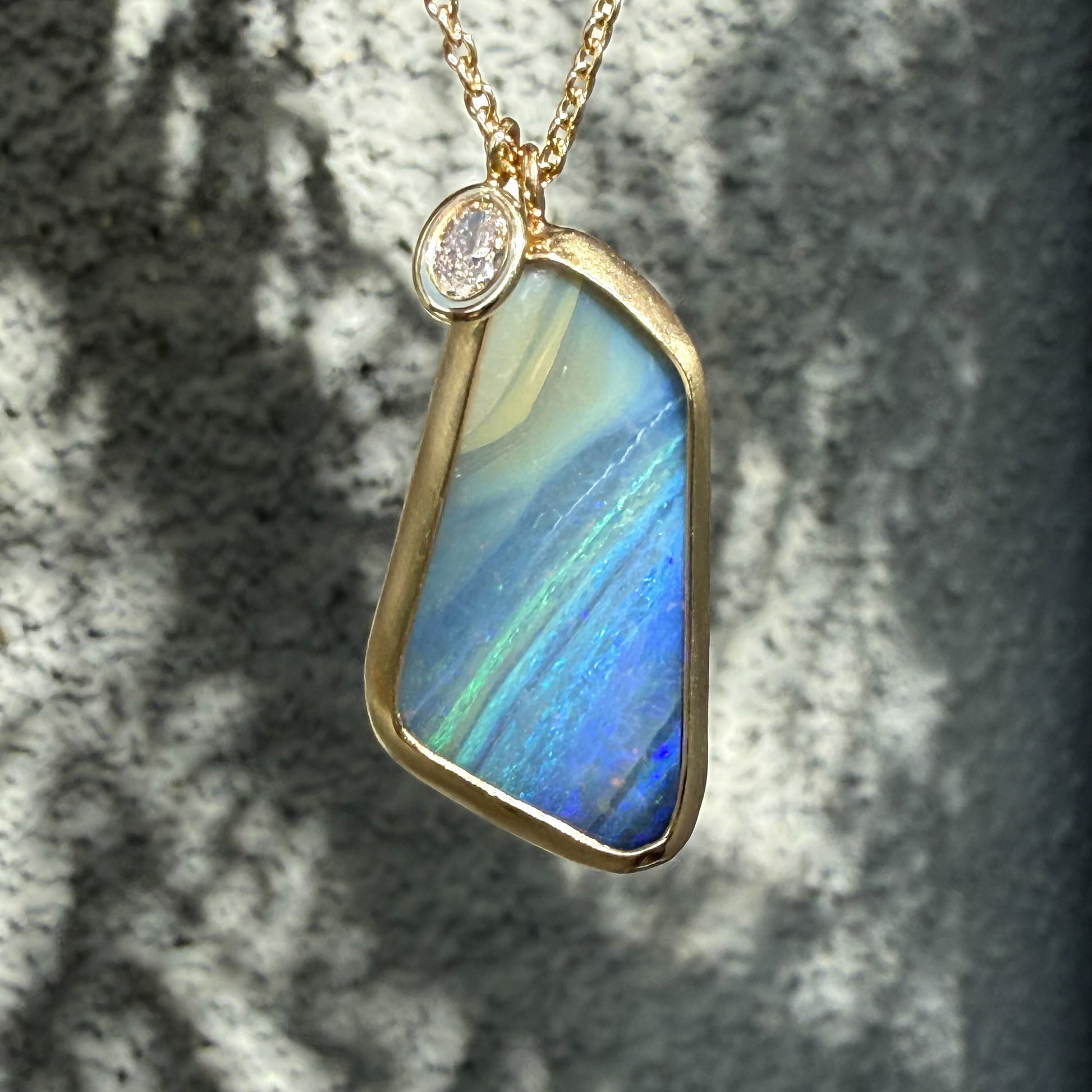 An Australian Opal Necklace by NIXIN Jewelry shown in sunlit shadow, emphasizing the natural opal and the gold chain. This rare jewelry employs a minimal bezel set design to maximize the visibility of the opal pendant.