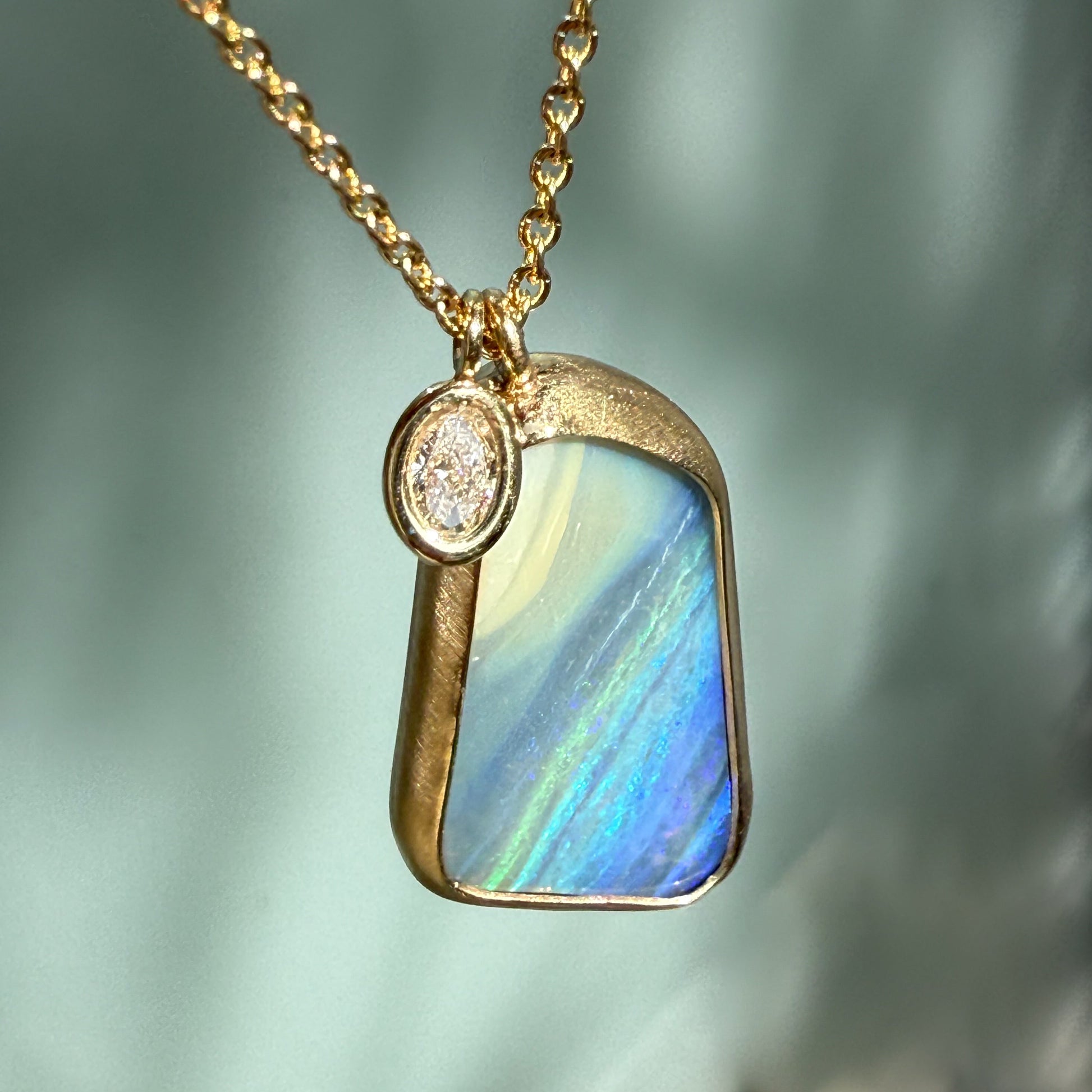 An Australian Opal Necklace by NIXIN Jewelry close-up focusing on the opal pendant's blue saturation and matte finish. This luxury jewelry is an example of art made with boulder opal. The charm is a brilliant, subtle diamond accent.