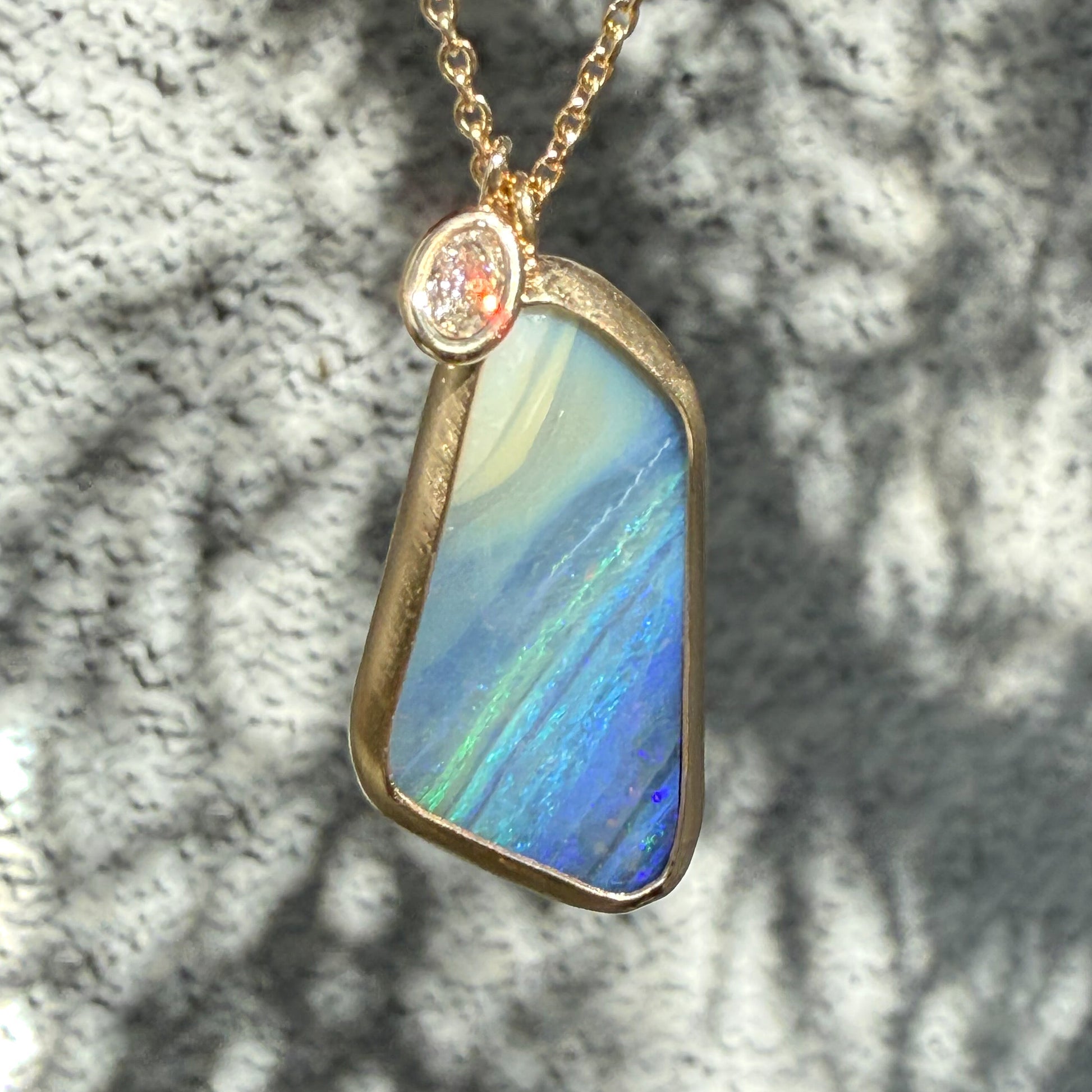 An Australian Opal Necklace by NIXIN Jewelry showing the bright shimmering color veins across the boulder opal. The unique opal jewelry is paired with a bezel setting diamond charm sparkling in the sunlight.