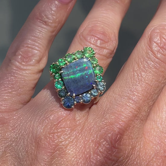 Video of an Australian Opal Ring by NIXIN Jewelry modeled on a hand. Features a blue opal ring with sapphires, emeralds and garnets.