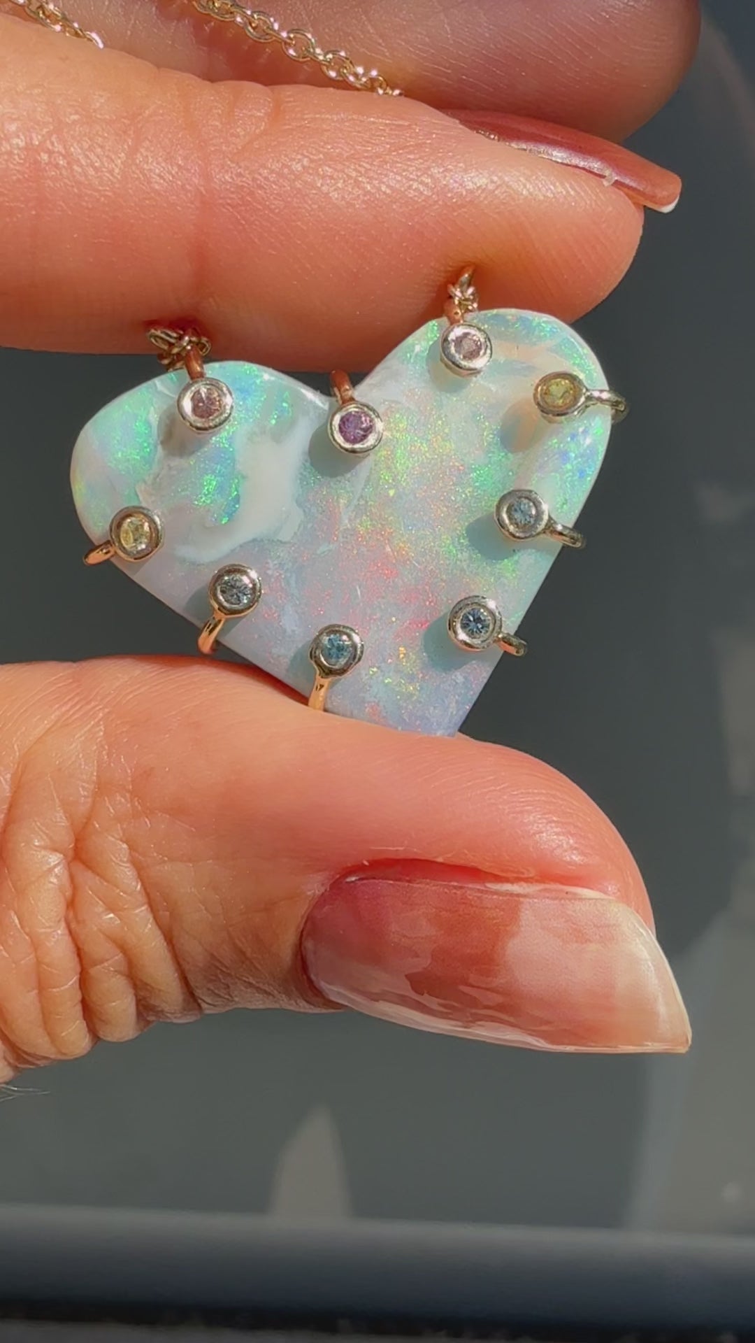 An Australian Opal Necklace by NIXIN Jewelry video capturing the play-of-color across the heart-shaped opal pendant in direct sunlight. The movement demonstrates the lightning ridge opal shifting from green and blue to red and pink flashes. This highly desirable unique opal jewelry piece is optimized for the luxury market.