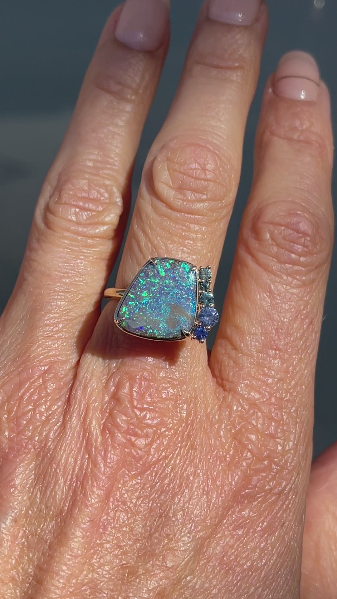 Video of an Australian Opal Ring by NIXIN Jewelry modeled on a hand. The opal and sapphire ring is made in yellow gold.