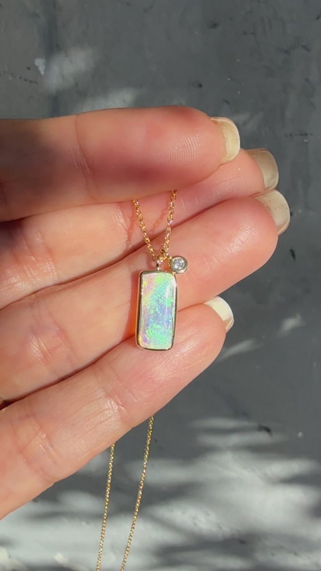 A video showing an Australian Opal Necklace by NIXIN Jewelry in sunlight. The video captures the play-of-color within the crystal opal stone as it moves. The footage highlights the detailed gold setting, the bezel-set diamond, and the craftsmanship of this luxurious opal pendant.