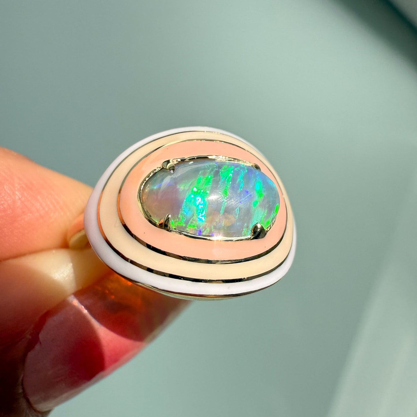 Close up of an Australian Opal Ring by NIXIN Jewelry, showcasing the opal's bright green and blue play-of-color. This gold opal ring features a beautiful prong setting and a bold enamel halo, perfect for those seeking unique opal jewelry.