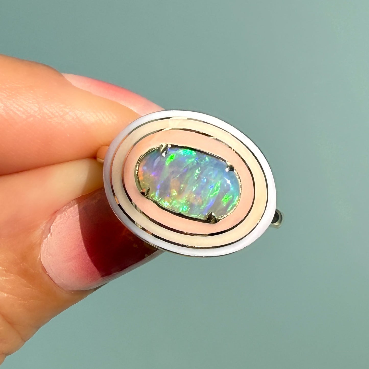 An Australian Opal Ring by NIXIN Jewelry, highlighting a radiant crystal opal with fiery neon green flashes. This unique opal ring, shown held against a teal background, is a modern and elegant piece of women's luxury jewelry.