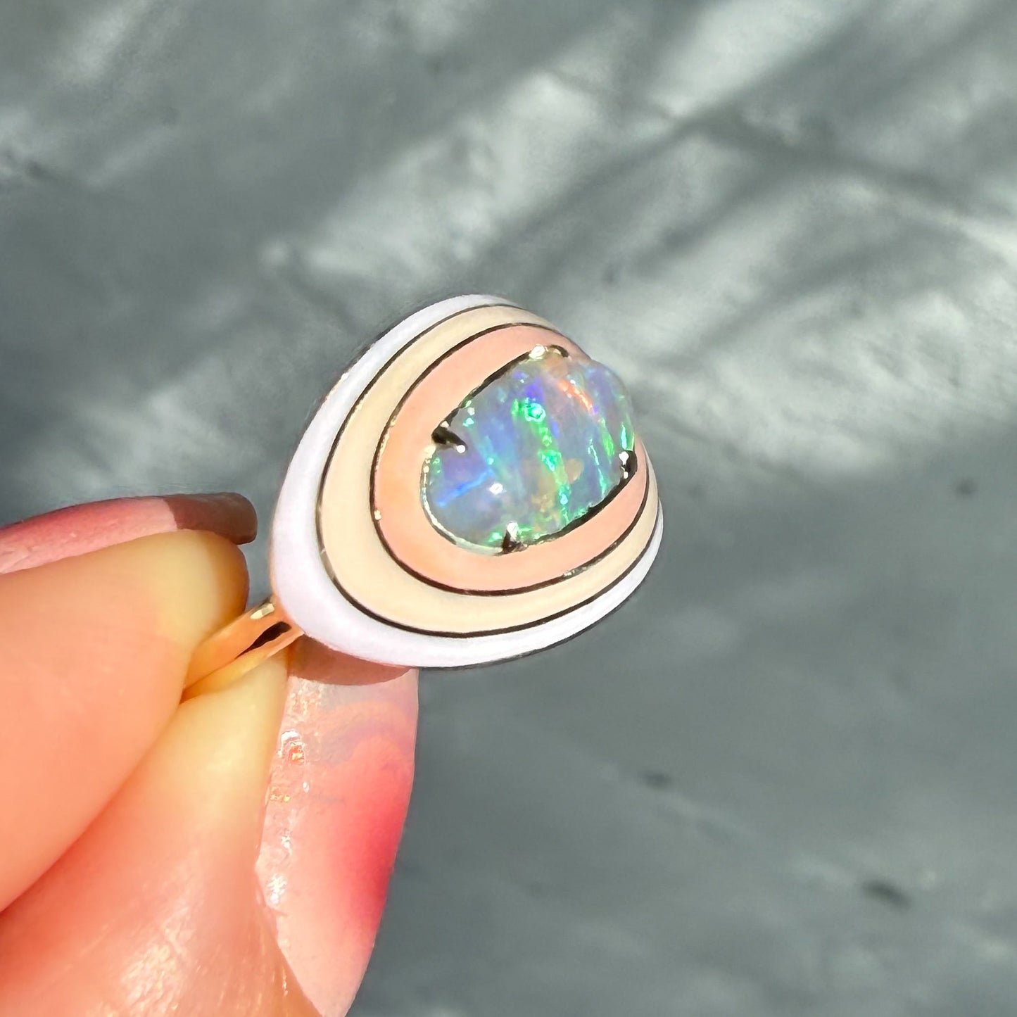 An Australian Opal Ring by NIXIN Jewelry, shown in a side profile view against a gray background. This modern opal ring features a central crystal opal and a multi-colored enamel halo, making it a truly unique fine jewelry piece.
