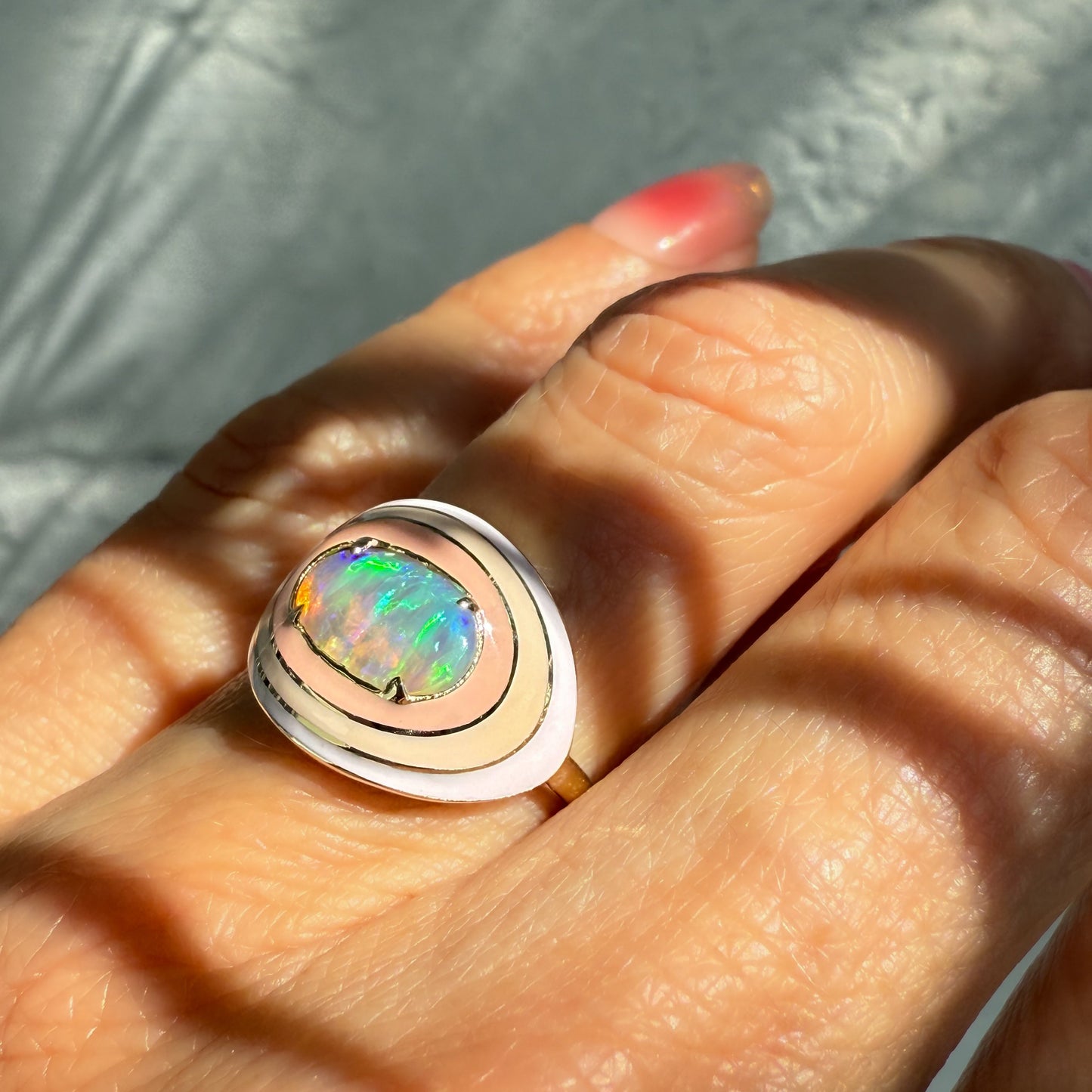 An Australian Opal Ring by NIXIN Jewelry, shown on a finger with light casting long shadows. This unique opal jewelry piece is a stunning example of a ladies opal ring, showcasing a vibrant lightning ridge opal in natural light.