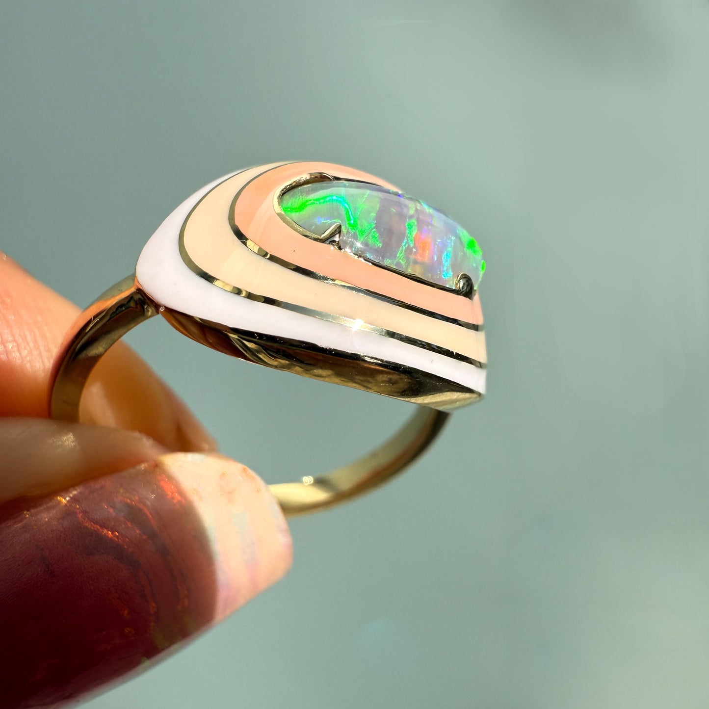 An angled shot of an Australian Opal Ring by NIXIN Jewelry, capturing the brilliant glow of the crystal opal. This gold opal ring is set against a textured light teal background, perfectly highlighting the unique design and the opal stone's natural beauty.