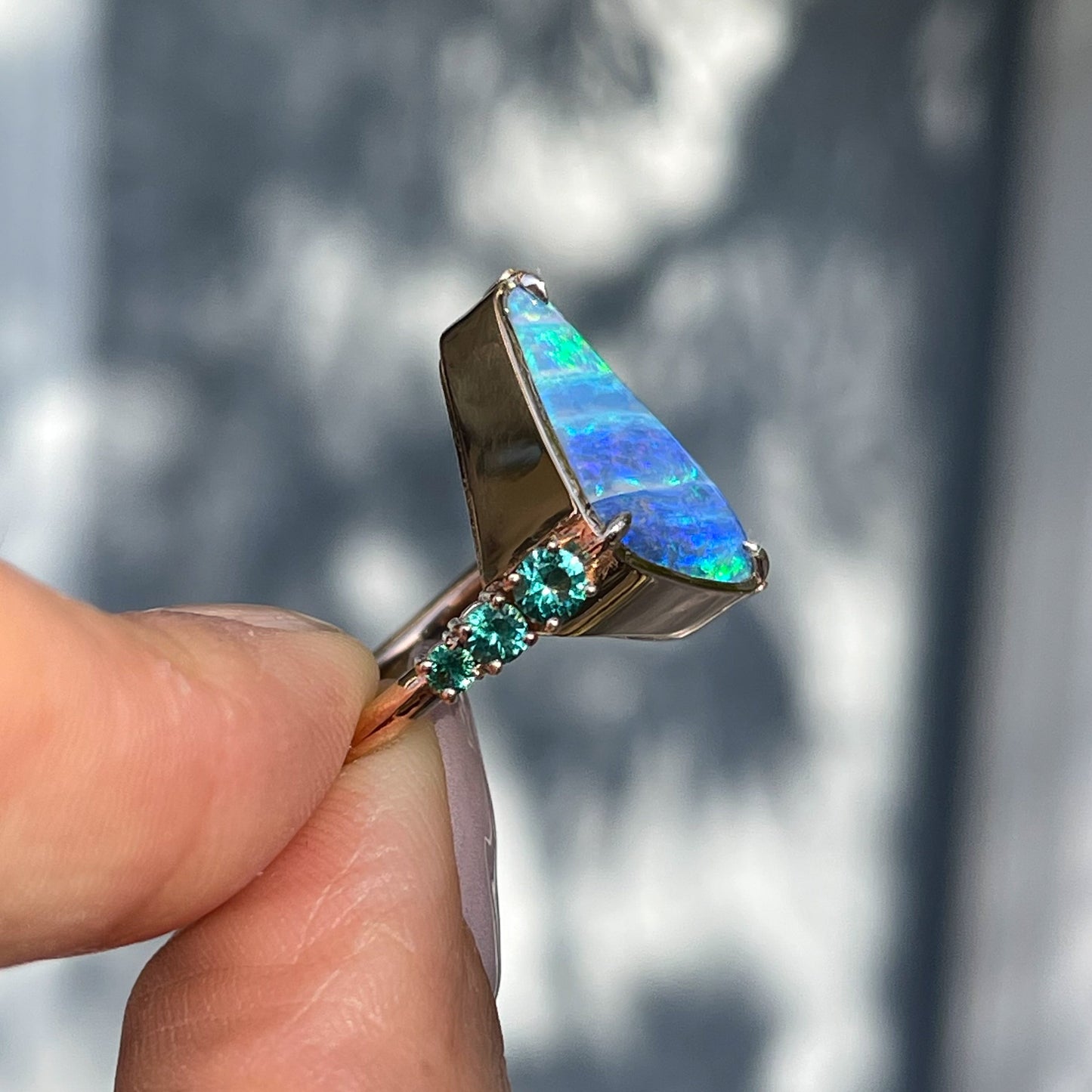 Side view of an Australian Opal Ring by NIXIN Jewelry showing emeralds in prong setting.