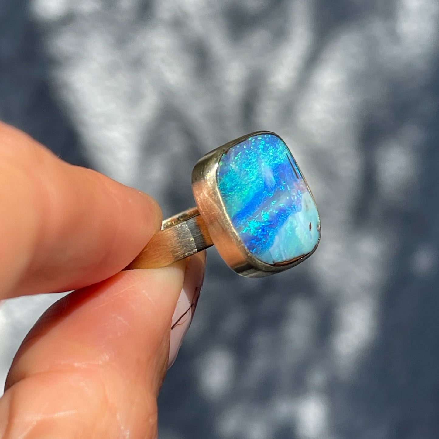 Side view of an Australian Opal Ring by NIXIN Jewelry. Shows the bezel setting holding the blue opal.