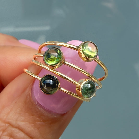Lucky Green Tourmaline Rings held on a fingertip, four 14k gold stacking rings showing the range of green tourmaline hues.