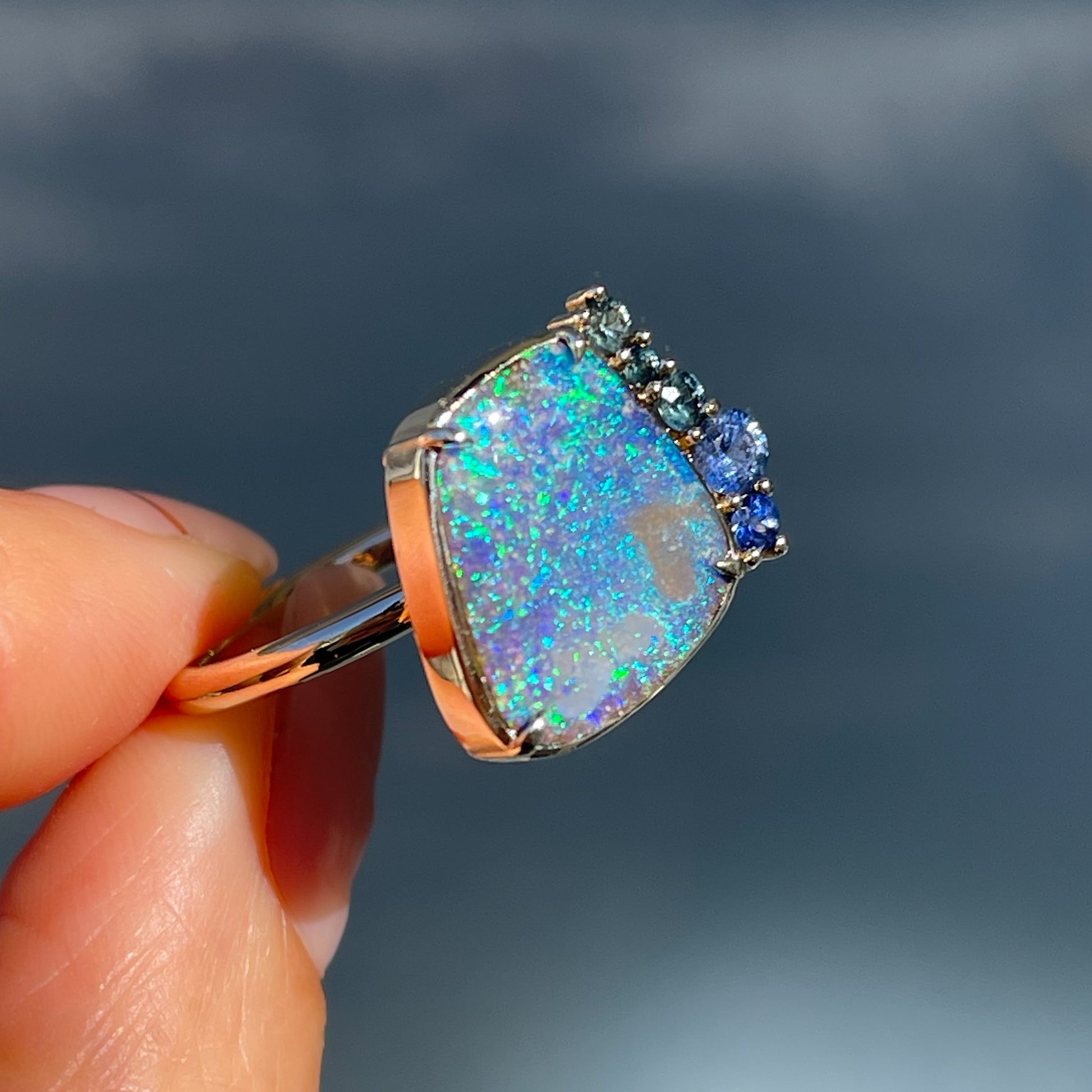 Angled view of an Australian Opal Ring by NIXIN Jewelry. A boulder opal ring with green and blue sapphires.