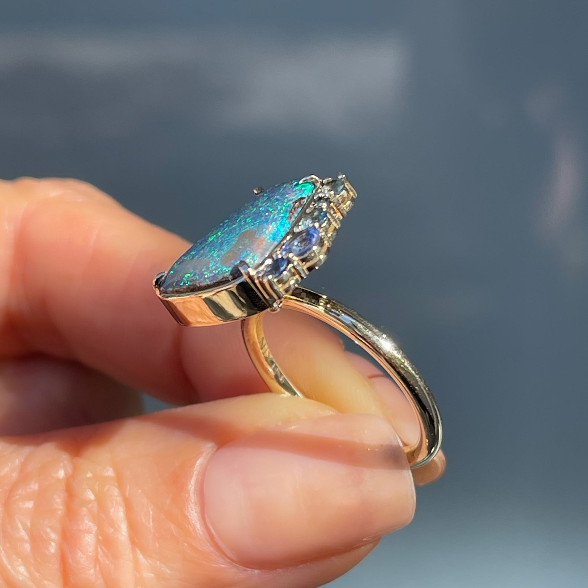 Angled shot of an Australian Opal Ring by NIXIN Jewelry. Shows the prong setting of the opal and sapphires and the gold band.