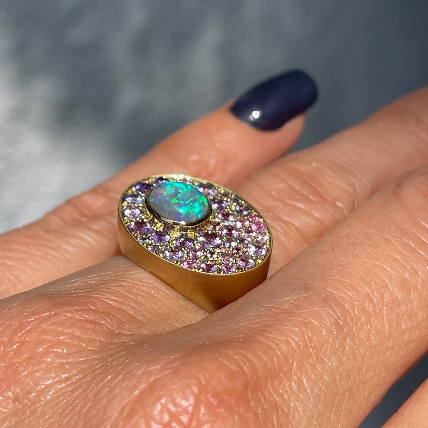 An Australian Opal Ring by NIXIN Jewelry shown in profile worn on the hand. The gold opal ring has a bezel set Crystal Opal and pave sapphires.