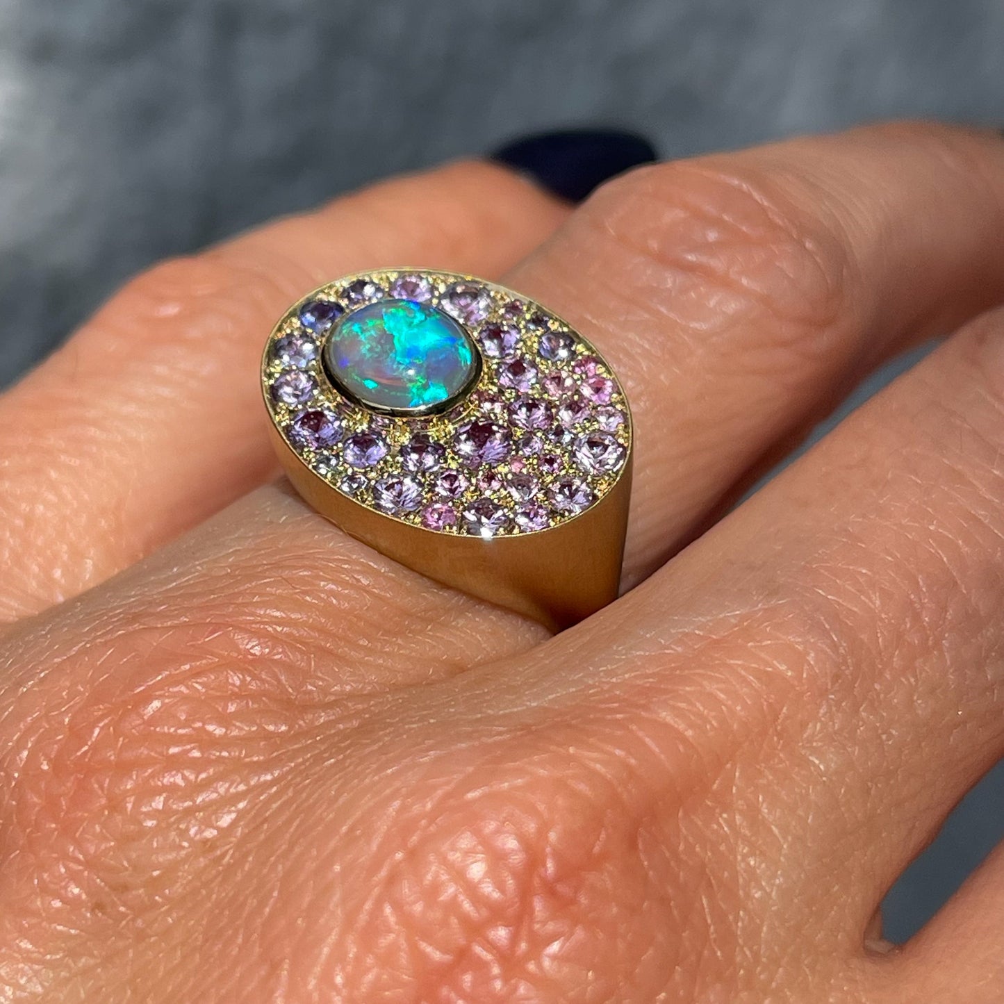 An Australian Opal Ring by NIXIN Jewelry is modeled on the hand and shown up close. Artisan jewelry made with sapphires and opal set in gold.