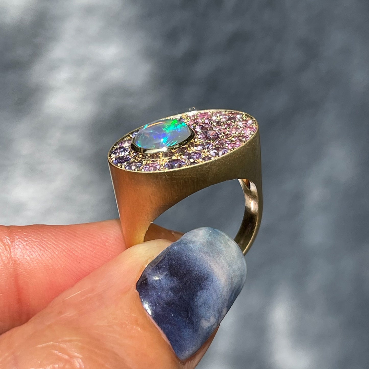 An Australian Opal Ring by NIXIN Jewelry held up to show its profile. The opal signet ring is made in 14k gold with ombré sapphires.