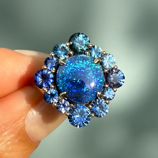 An Australian Opal Ring by NIXIN Jewelry. A close-up shot highlights the intense blue and green play-of-color in the natural opal, set in a brilliant sapphire and opal ring. This women's luxury ring is considered unique fine jewelry, perfect for those seeking black opal jewelry and a statement cocktail ring.